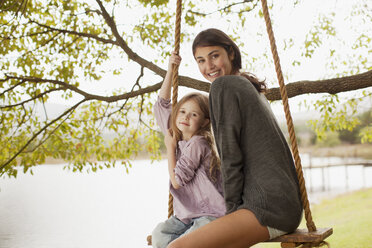 Portrait of mother and daughter on swing at lakeside - CAIF00137