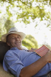 Porträt eines lächelnden Mannes, der mit einem Buch im Gras liegt - CAIF00139