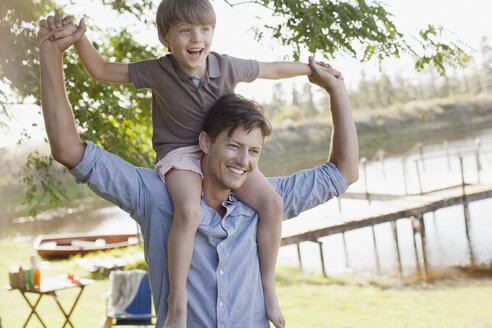 Vater trägt lächelnden Sohn auf den Schultern am Seeufer - CAIF00144