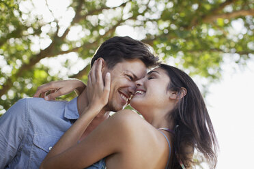 Smiling couple hugging under tree - CAIF00149