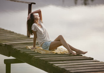 Woman with head back and hand in hair on dock over lake - CAIF00164