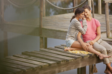 Affectionate couple sitting on dock over lake - CAIF00182