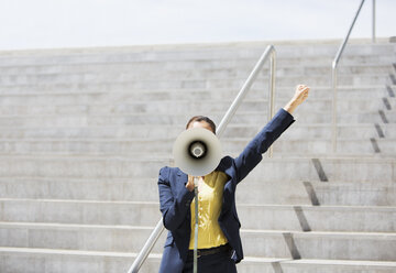 Businesswoman using megaphone on urban steps - CAIF00224