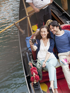 Lächelndes Paar beim Fotografieren in einer Gondel auf einem Kanal in Venedig - CAIF00317