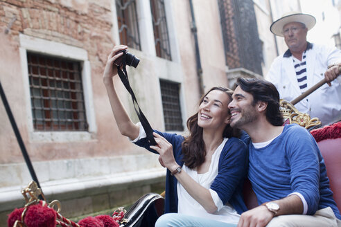 Lächelndes Paar, das sich mit einer Digitalkamera in einer Gondel auf einem Kanal in Venedig selbst porträtiert - CAIF00321