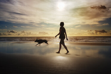 Silhouette einer Frau und eines Hundes, die am Strand spazieren gehen - CAIF00444