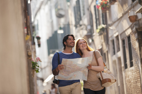 Lächelndes Paar mit Karte in einer engen Straße in Venedig, lizenzfreies Stockfoto