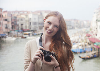 Porträt einer lächelnden Frau mit Digitalkamera am Hafen von Venedig - CAIF00471