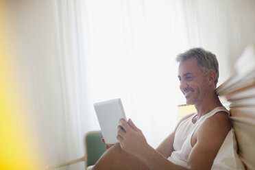 Lächelnder Mann mit digitalem Tablet im Bett - CAIF00507