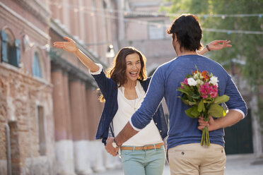 Enthusiastische Frau nähert sich Mann mit Blumen hinter dem Rücken - CAIF00524