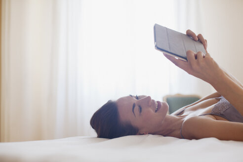Lächelnde Frau, die auf dem Bett liegt und ein digitales Tablet benutzt - CAIF00525