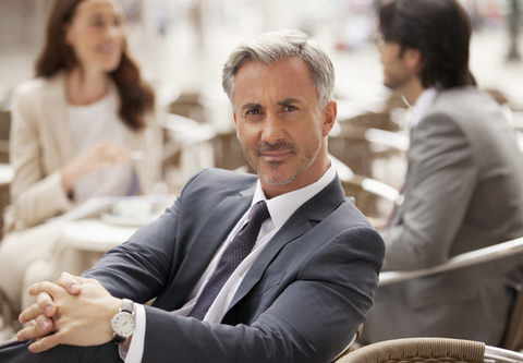 Porträt eines lächelnden Geschäftsmannes in einem Straßencafé mit Mitarbeitern im Hintergrund, lizenzfreies Stockfoto