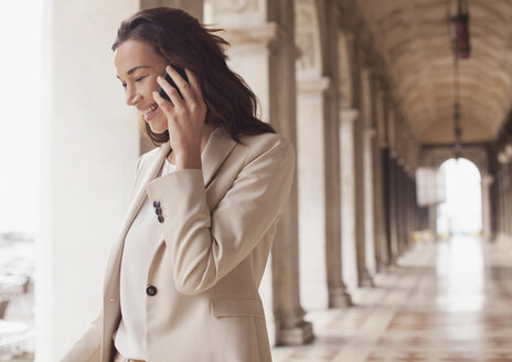Lächelnde Geschäftsfrau, die im Korridor mit einem Handy telefoniert - CAIF00559
