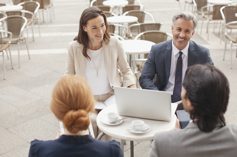 Lächelnde Geschäftsleute mit Laptop treffen sich in einem Straßencafé, lizenzfreies Stockfoto