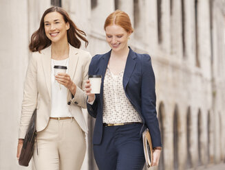 Smiling businesswomen walking with coffee - CAIF00586