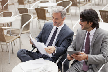 Lächelnde Geschäftsleute mit digitalem Tablet und Papierkram in einem Cafe - CAIF00589