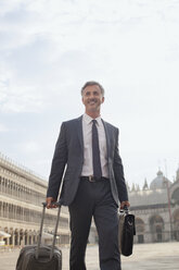 Smiling businessman pulling suitcase through Saint Mark's Square in Venice - CAIF00601