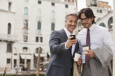 Lächelnde Geschäftsleute mit Kaffee schauen auf ihr Handy in Venedig - CAIF00604