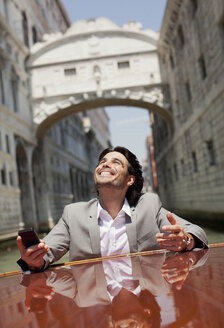 Enthusiastischer Geschäftsmann fährt auf einem Boot durch einen Kanal in Venedig - CAIF00608