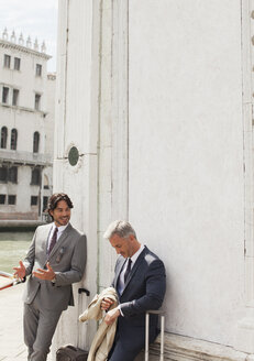 Geschäftsleute mit Koffern, die sich unterhalten und an ein Gebäude in Venedig lehnen - CAIF00609