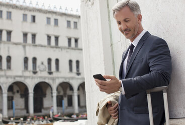 Geschäftsmann blickt in Venedig auf sein Handy - CAIF00614