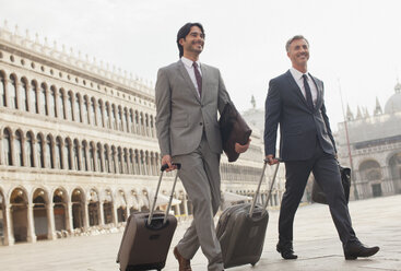 Lächelnde Geschäftsleute gehen mit Koffern über den Markusplatz in Venedig - CAIF00616
