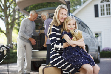 Smiling mother and daughter sitting on luggage - CAIF00686