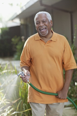Ältere Männer gießen Pflanzen im Hinterhof, lizenzfreies Stockfoto