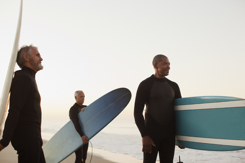 Ältere Surfer tragen Bretter am Strand, lizenzfreies Stockfoto