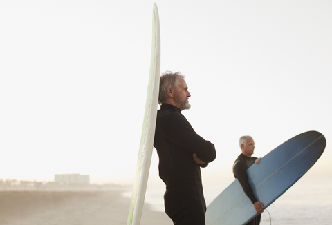 Älterer Surfer lehnt sich am Strand an sein Brett, lizenzfreies Stockfoto