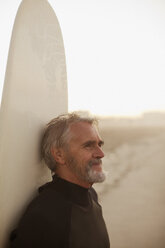 Älterer Surfer lehnt sich am Strand an sein Brett - CAIF00880