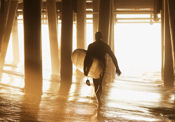 Älterer Surfer trägt Brett unter dem Pier - CAIF00887