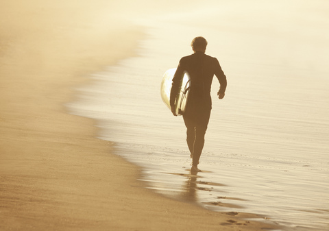 Älterer Surfer mit Brett am Strand, lizenzfreies Stockfoto