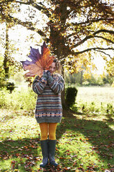 Girl playing with autumn leaf outdoors - CAIF00903