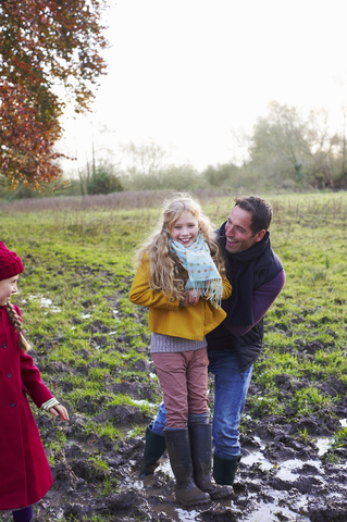 Vater und Tochter lachen auf einem schlammigen Feld, lizenzfreies Stockfoto