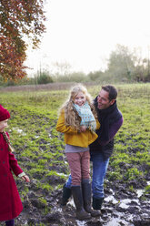 Father and daughter laughing in muddy field - CAIF00921