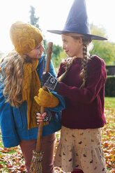 Girls playing with witch's hat and broom outdoors - CAIF00940