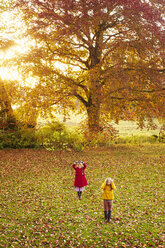 Girls playing in field of autumn leaves - CAIF00948