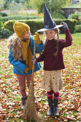 Girls playing with witch's hat and broom outdoors - CAIF00955