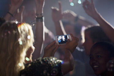 Frau mit Fotohandy fotografiert Freunde auf der Tanzfläche eines Nachtclubs - CAIF01050
