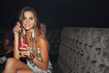 Portrait of smiling woman drinking cocktail in nightclub - CAIF01077