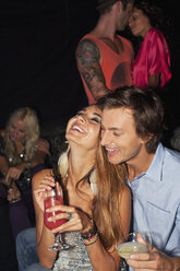 Lachendes Paar, das sich umarmt und Cocktails in einem Nachtclub trinkt - CAIF01088