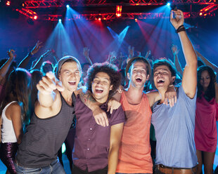 Enthusiastic friends cheering on dance floor of nightclub - CAIF01089