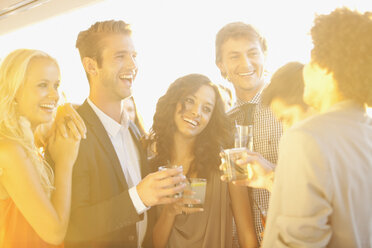 Lächelnde Freunde trinken Cocktails auf einem sonnigen Balkon - CAIF01112