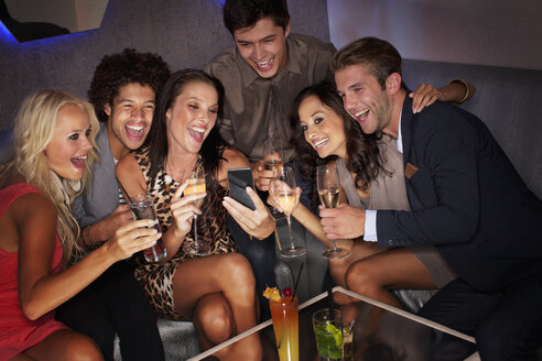 Lächelnde Freunde trinken Cocktails und schauen auf ihr Handy in einem Nachtclub - CAIF01117