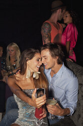 Lächelndes Paar trinkt Cocktails und macht ein Selbstporträt mit Fotohandy in einem Nachtclub - CAIF01120