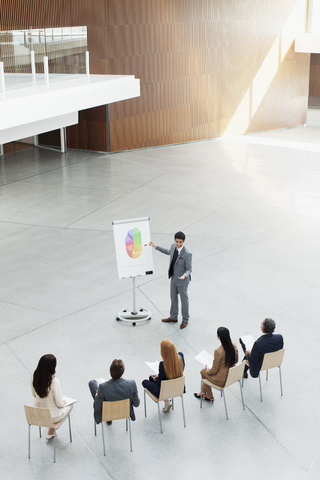 Geschäftsmann am Flipchart, der eine Sitzung in einer modernen Lobby leitet, lizenzfreies Stockfoto