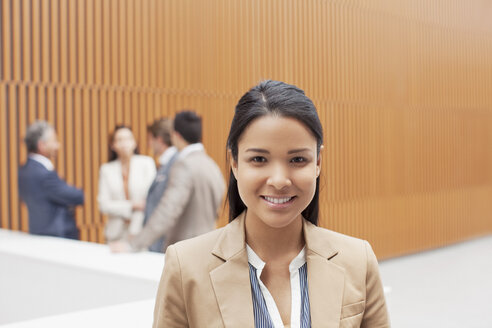 Porträt einer lächelnden Geschäftsfrau mit einer Besprechung von Mitarbeitern im Hintergrund - CAIF01135