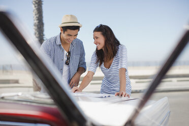 Smiling couple reading road map on convertible - CAIF01156