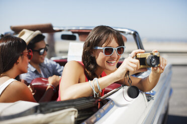 Smiling woman taking picture from convertible - CAIF01158